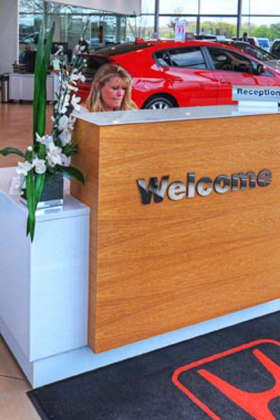 The inside of a Honda car showroom with a blonde woman sat behind the 'Welcome' desk.