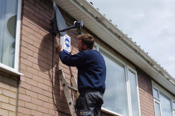 A man installing an Amthal burglar alarm to the outside wall of a house.