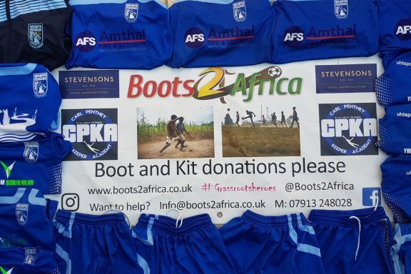 Boots2Africa charity sign surrounded by blue football shirts displaying the Amthal company logo.