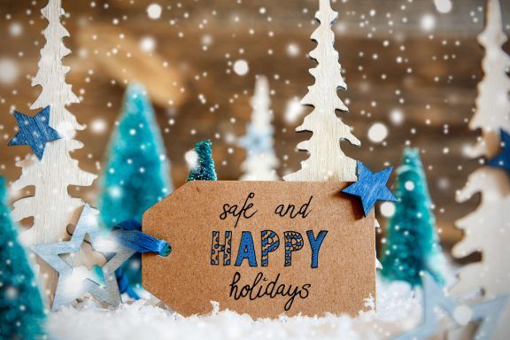 A Christmas gift tag with 'safe and happy holidays' written on it, surrounded by cardboard Christmas trees.