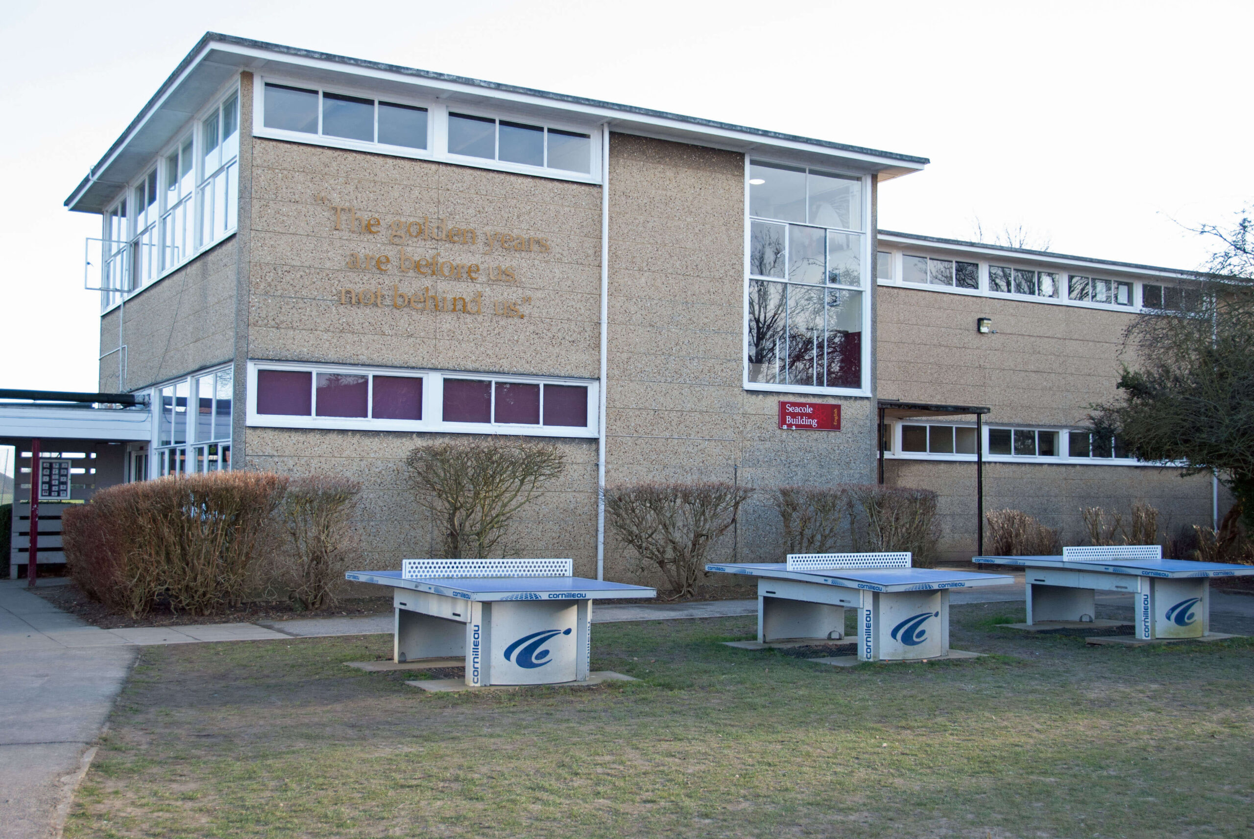 A school building with concrete table tennis tables in the foreground.
