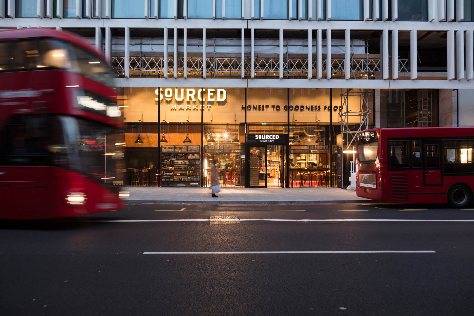 A glass-fronted shop with red buses driving past in the foreground.