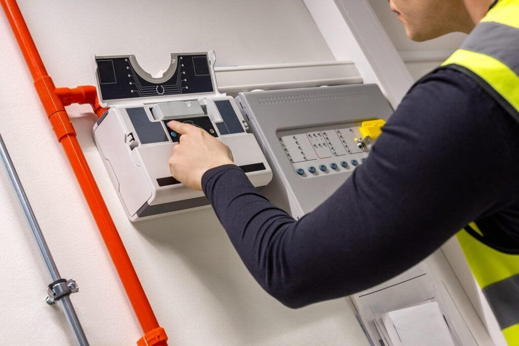 An Amthal employee wearing a high-vis jacket inspecting a fire alarm system.