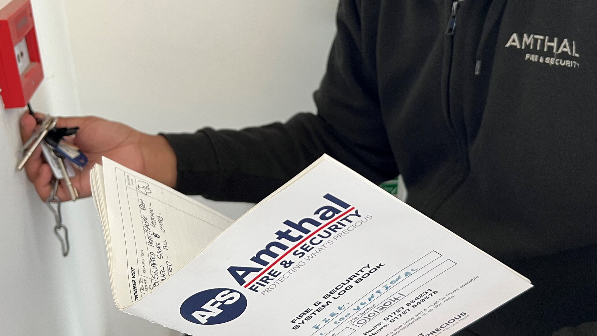An Amthal employee wearing a black fleece with the Amthal company logo, while reading an Amthal Fire & Security document.